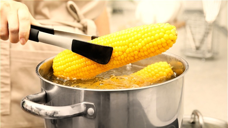 Tongs removing corn cob from water