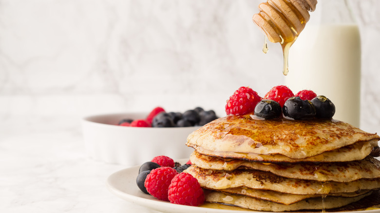 stack on pancakes topped with fruit and honey dripping