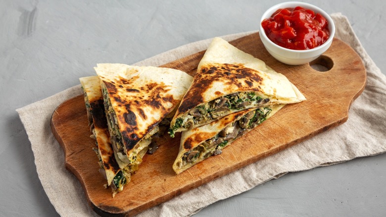 quesadilla with spinach and mushrooms on a wooden platter with a ketchup bowl