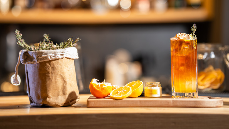 Cocktail on a bar top with slice of orange and bag of herbs