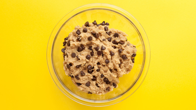 Chocolate chip cookie dough in clear bowl yellow background