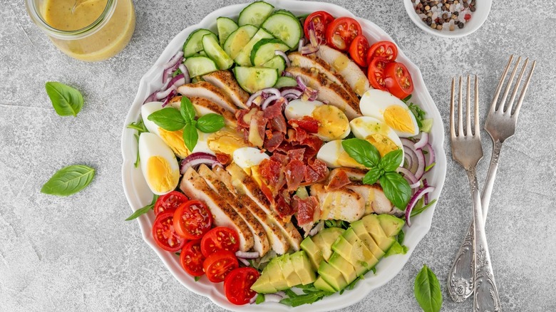 Cobb salad displayed on plate by dressing and silverware.