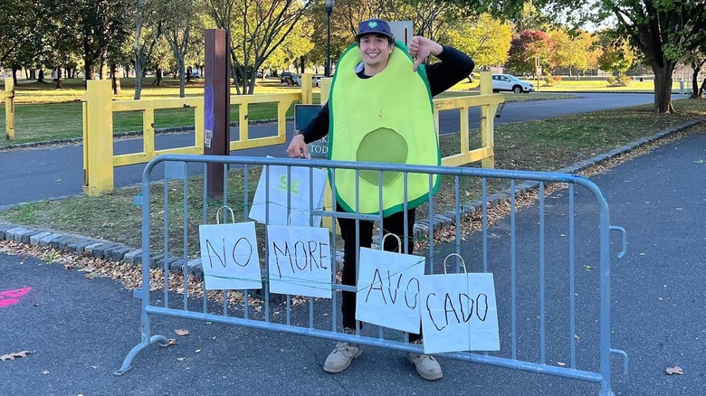 Sharing Excess volunteer in avocado costume stands in front of 'No more avocado' sign