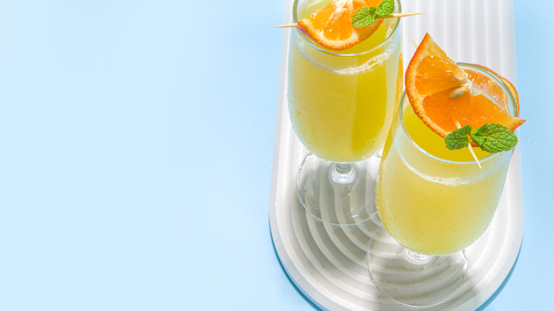 Two mimosas with orange garnishes.