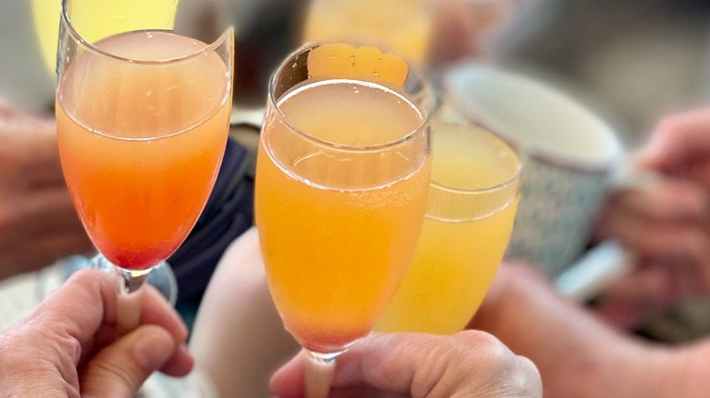 A variety of different mimosas being tapped togther in a 'cheers'