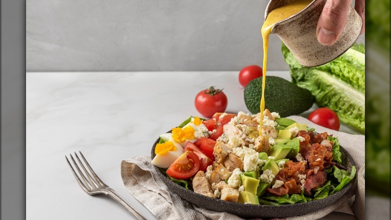 Pouring dressing over a Cobb Salad