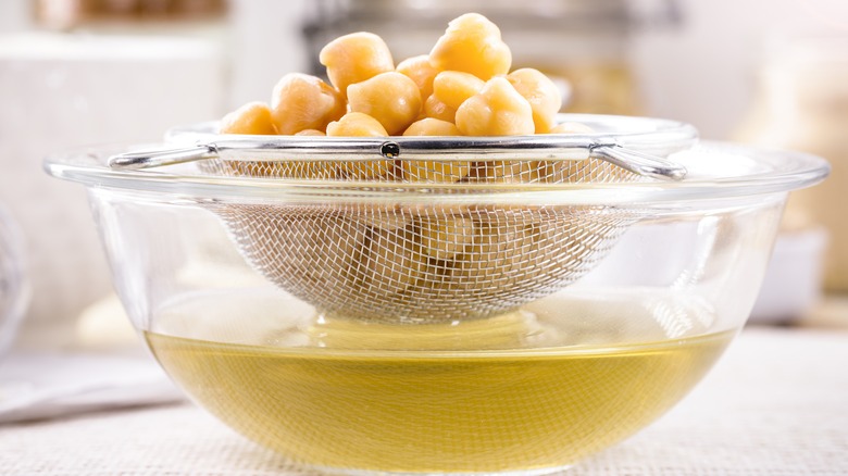 Bowl of aquafaba liquid under a mesh strainer full of chickpeas