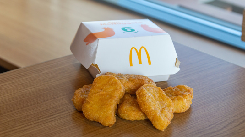 Six Chicken McNuggets piled outside of their white McDonald's box.