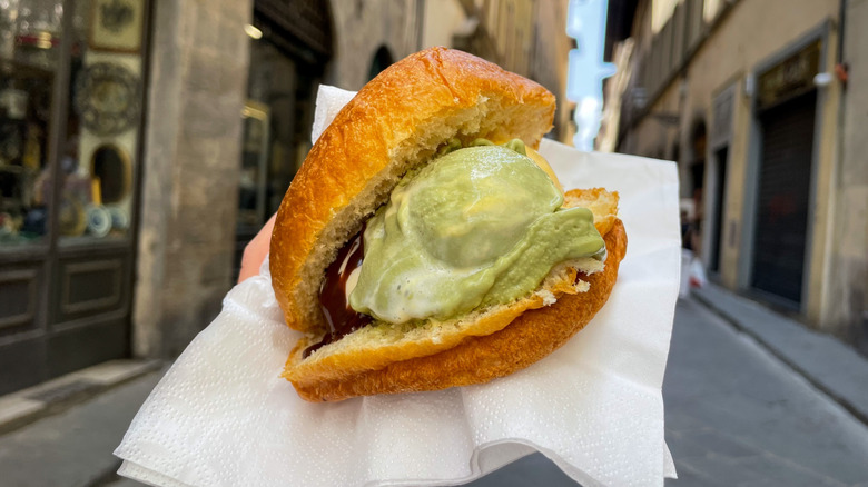 Hand holding gelato con brioche in a napkin