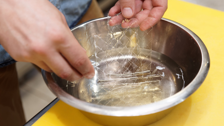 Hands mixing gelatin sheets with water in a metal bowl