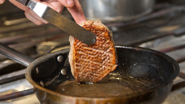 person flipping crispy skinned duck breast in a pan