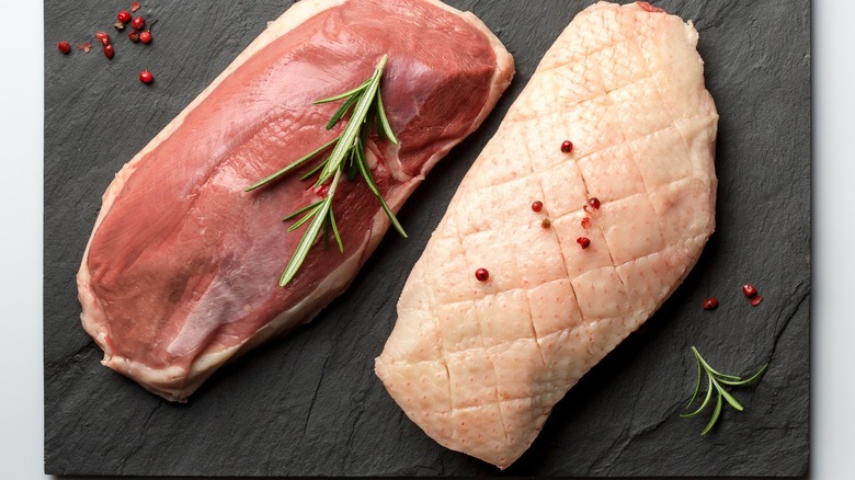 Raw seasoned duck breasts atop a cutting board