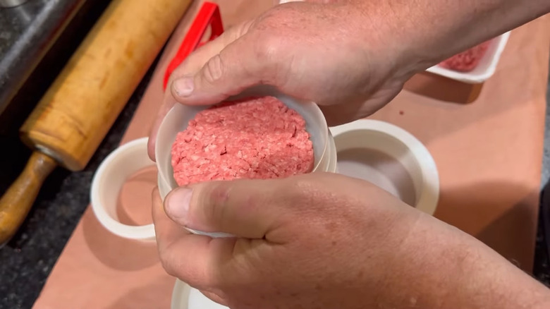 A person holding a tupperware lid with a burger