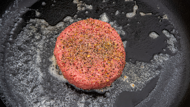 A seasoned burger cooking over melted butter