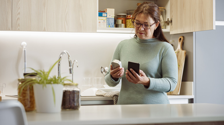 woman inspecting canned food with phone