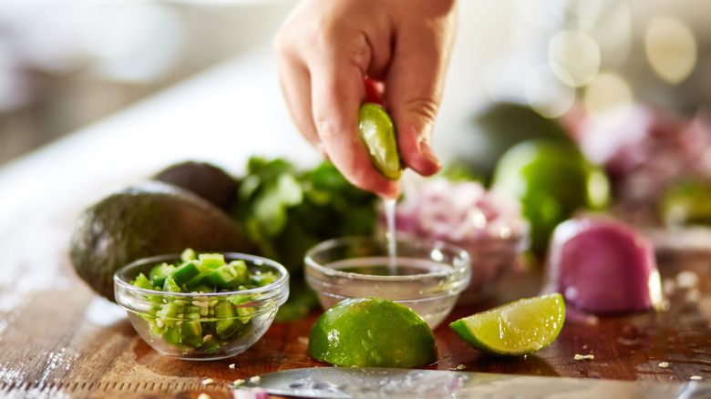 Person squeezing lime wedges into a bowl on a cutting board