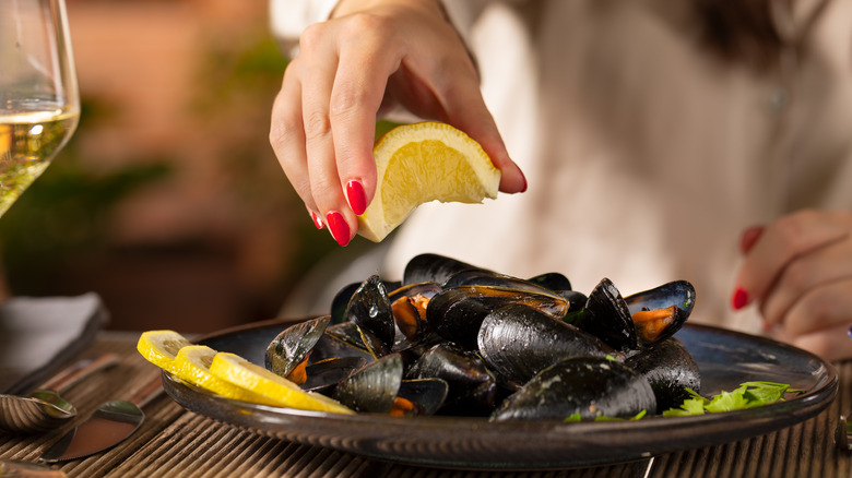 Woman squeezes a lemon wedge over a plate of mussels