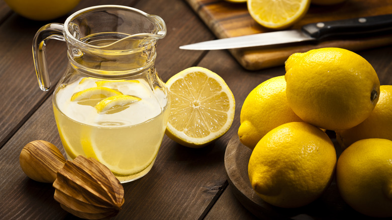 Whole lemons next to a pitcher of lemonade