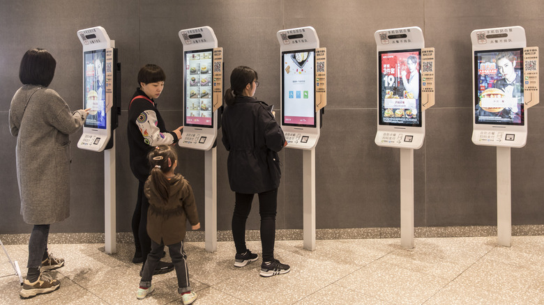 People stand at food ordering kiosks
