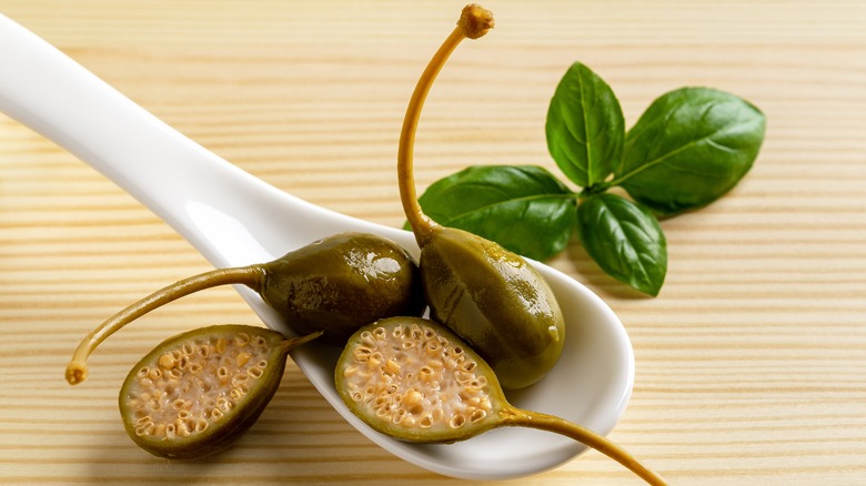 Caperberries on a spoon with basil in the background