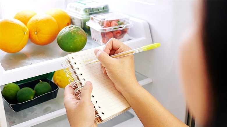 Hand writing grocery list in refrigerator 