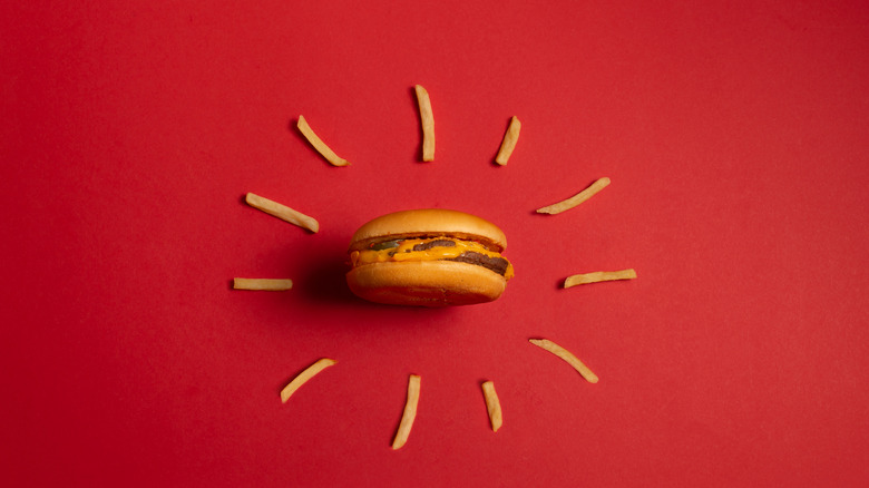 A hamburger surrounded by fries on a red background