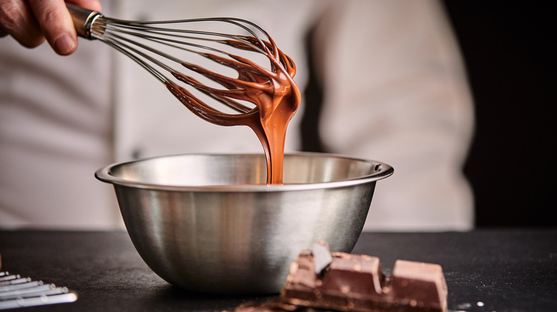 Baker swirling chocolate in a metal bowl