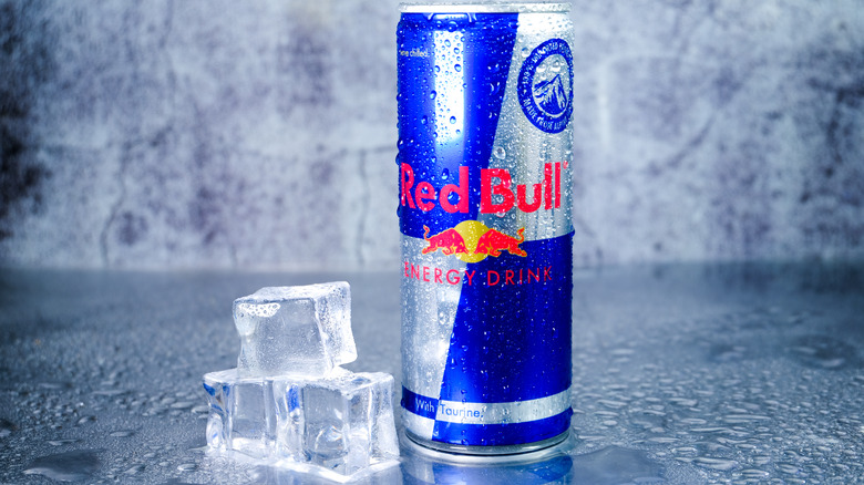 A can of Red Bull next to three ice cubes 