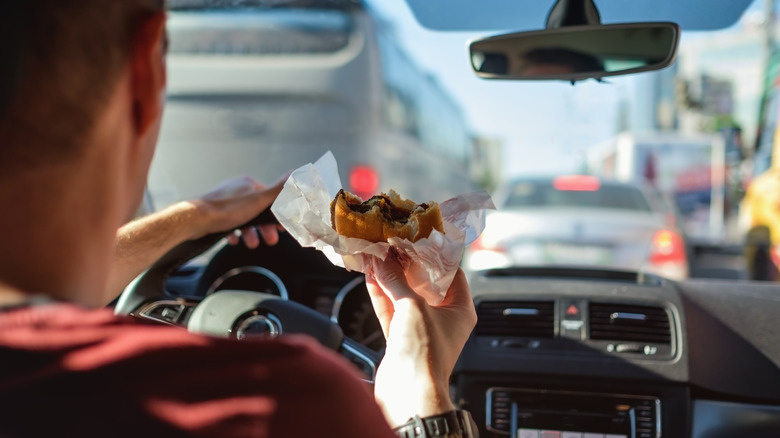 man eating fast food burger while driving