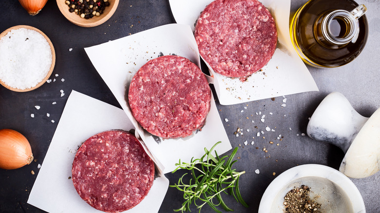 Seasoning raw burgers on counter