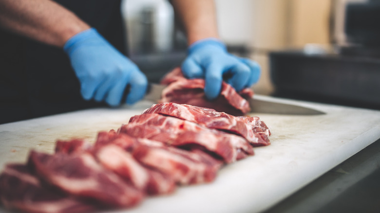 gloved hands cutting raw meat