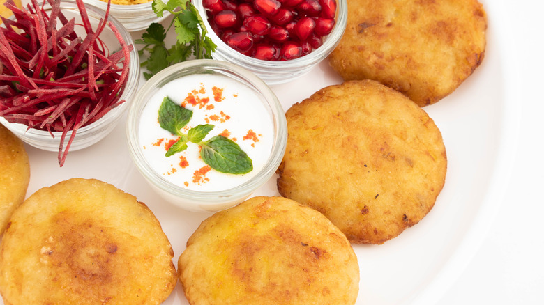 potato chop on a plate with raita and pomegranate seeds