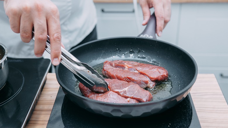 person cooking steak slices in pan