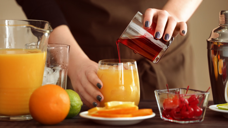 Hands making a batch of tequila sunrise drinks