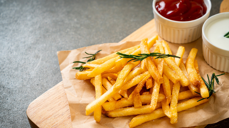 French fries and condiments on wooden tray