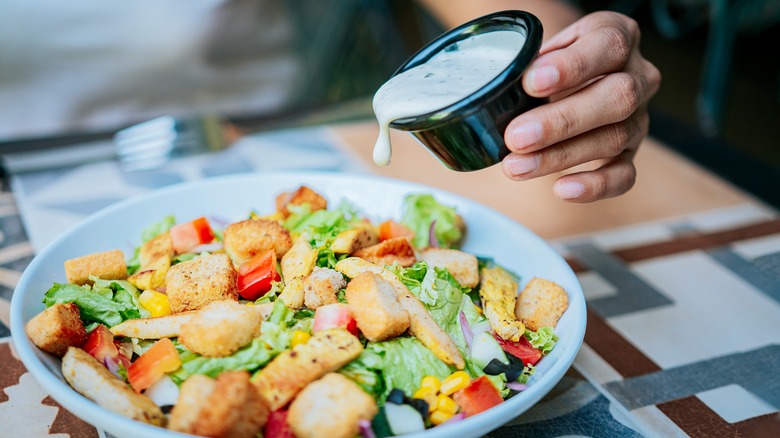 Hand pouring dressing on salad