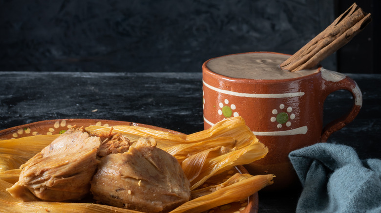 Champurrado, cinnamon sticks, and tamales surrounding a red mug