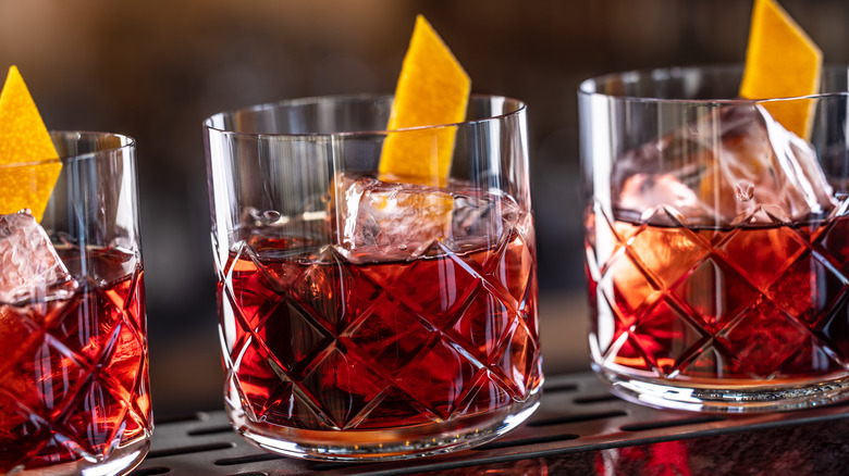 three glasses of Negroni with orange peels on ice