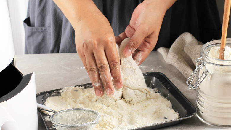 hands dredging pieces of chicken in flour