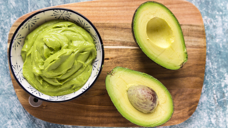 mashed avocado and two halves of avocado on wooden board