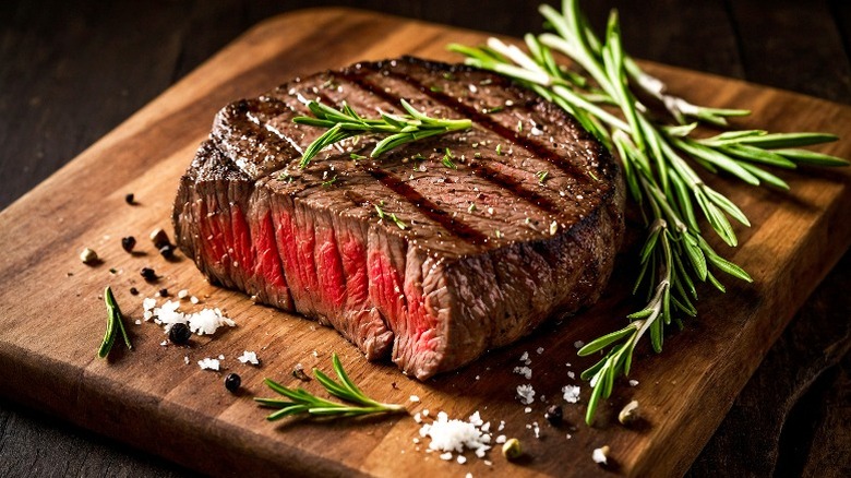 Medium-rare steak on a wooden cutting board with rosemary, salt, and pepper corns