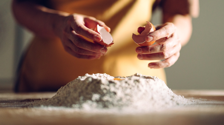 person holding cracked egg shell halves as they prepare pasta dough