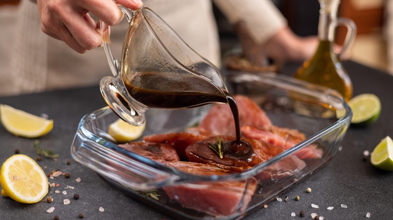 Person pouring marinade over meat in a glass dish