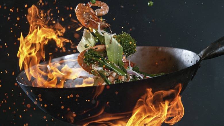 ingredients being tossed in a wok over a flame