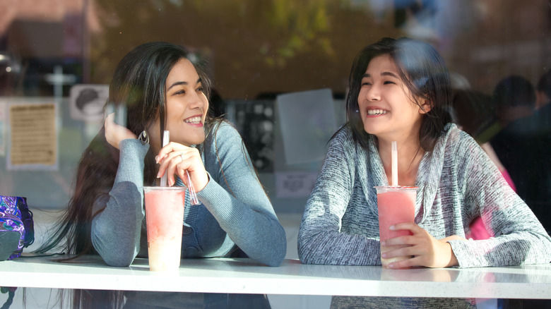 two girls drinking boba in window