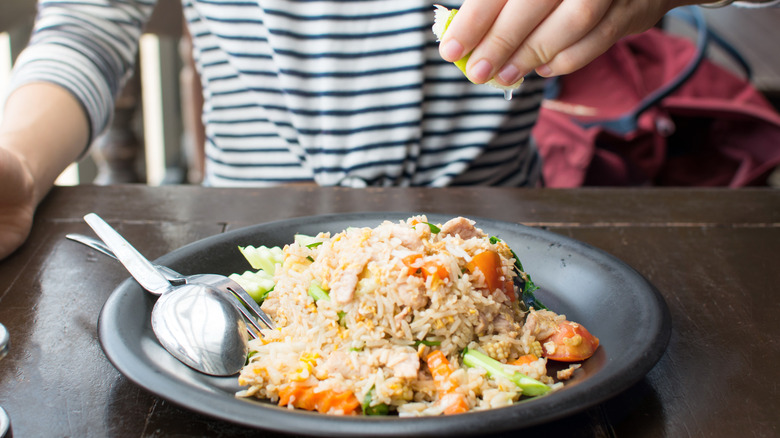 Woman squeezing lemon juice over baked rice