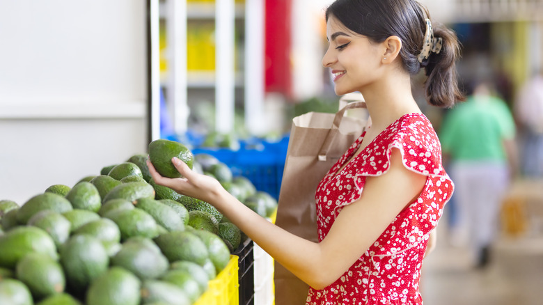 woman selecting avocados at supermarket