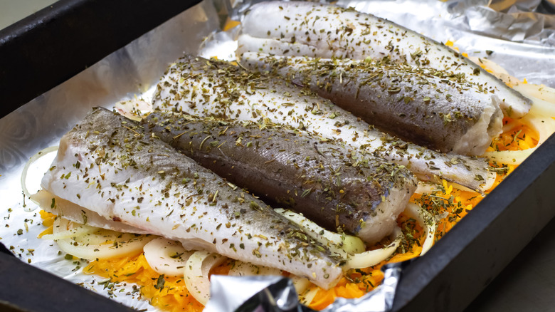 Five filets of silver hake fish, seasoned and resting on a bed of onions