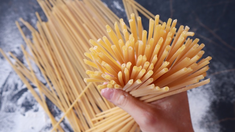 Hand holding uncooked bucatini pasta