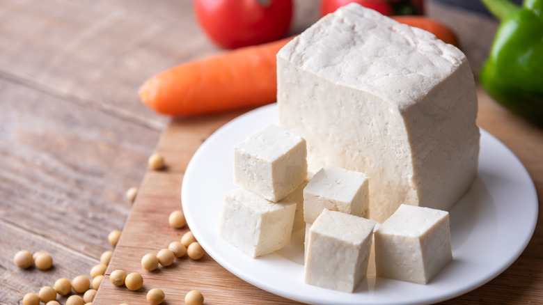 a large piece of fresh soft white tofu with some cut into cubes on a cutting board